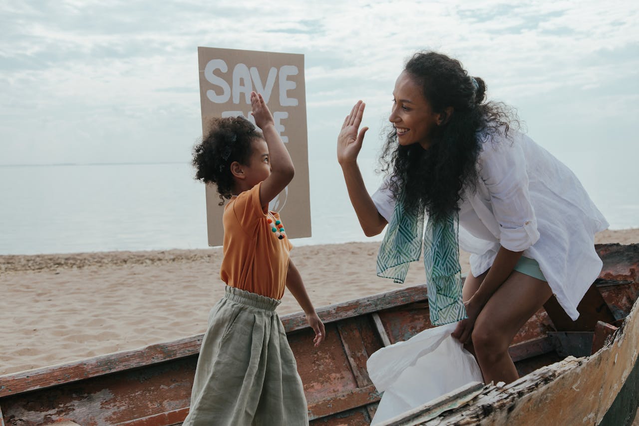 Mother and child high-five during a fun beach cleanup with a save the planet sign.